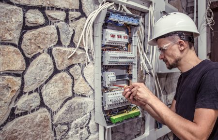 a male electrician works in a switchboard with an electrical connecting cable, connects the equipment with tools, the concept of complex work, space for text